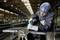 A worker in protective gear uses an electric tool to work on a large piece of metal in an industrial warehouse setting.