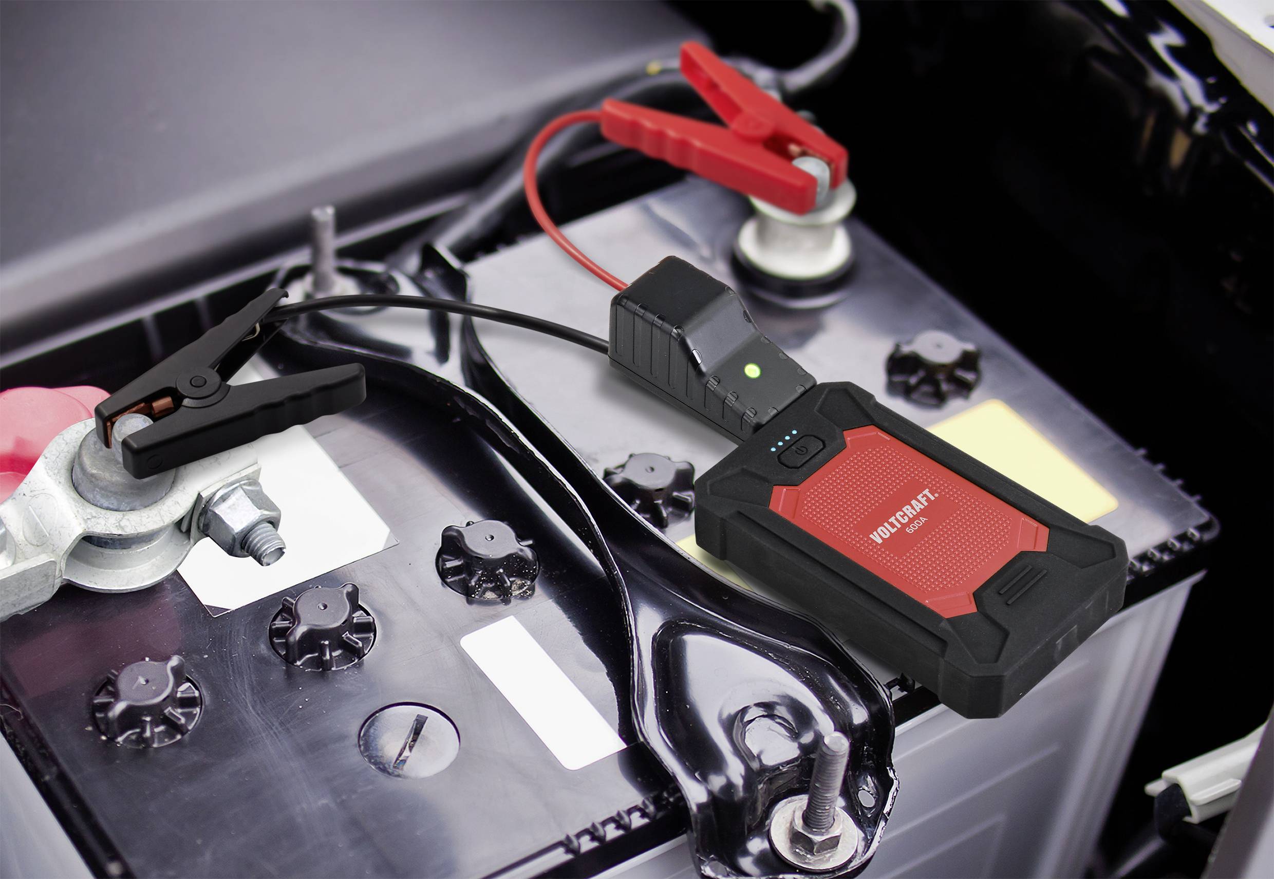 A red jump starter with charging cables lies on a car battery, ready to start a vehicle.