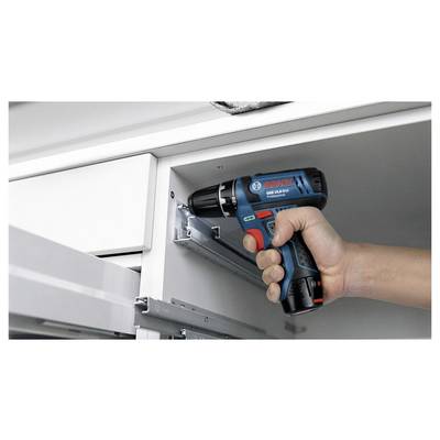 A person uses a blue and black cordless power drill to install a drawer slide on a white cabinet.