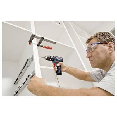A person installs metal drawer slides on wooden shelving using a power drill, wearing protective eyewear for safety.