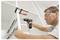A man wearing safety glasses uses a power drill to install cabinet fixtures in a white shelving unit.