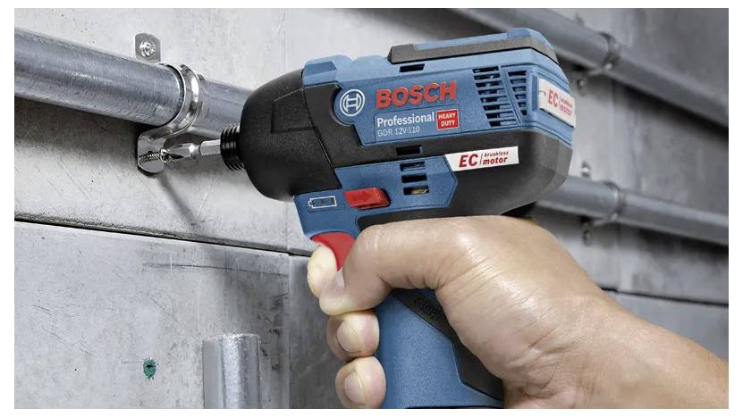 A hand holding a blue power drill with a red trigger is tightening a metal bolt on a concrete wall. The drill is marked 'BOSCH Professional.'