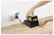 Hands placing a black and yellow battery onto a charger on a wooden surface, with the charger plugged into a wall socket.