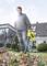 A man is standing in the garden using a yellow leaf blower to remove autumn leaves from the lawn in front of a house.