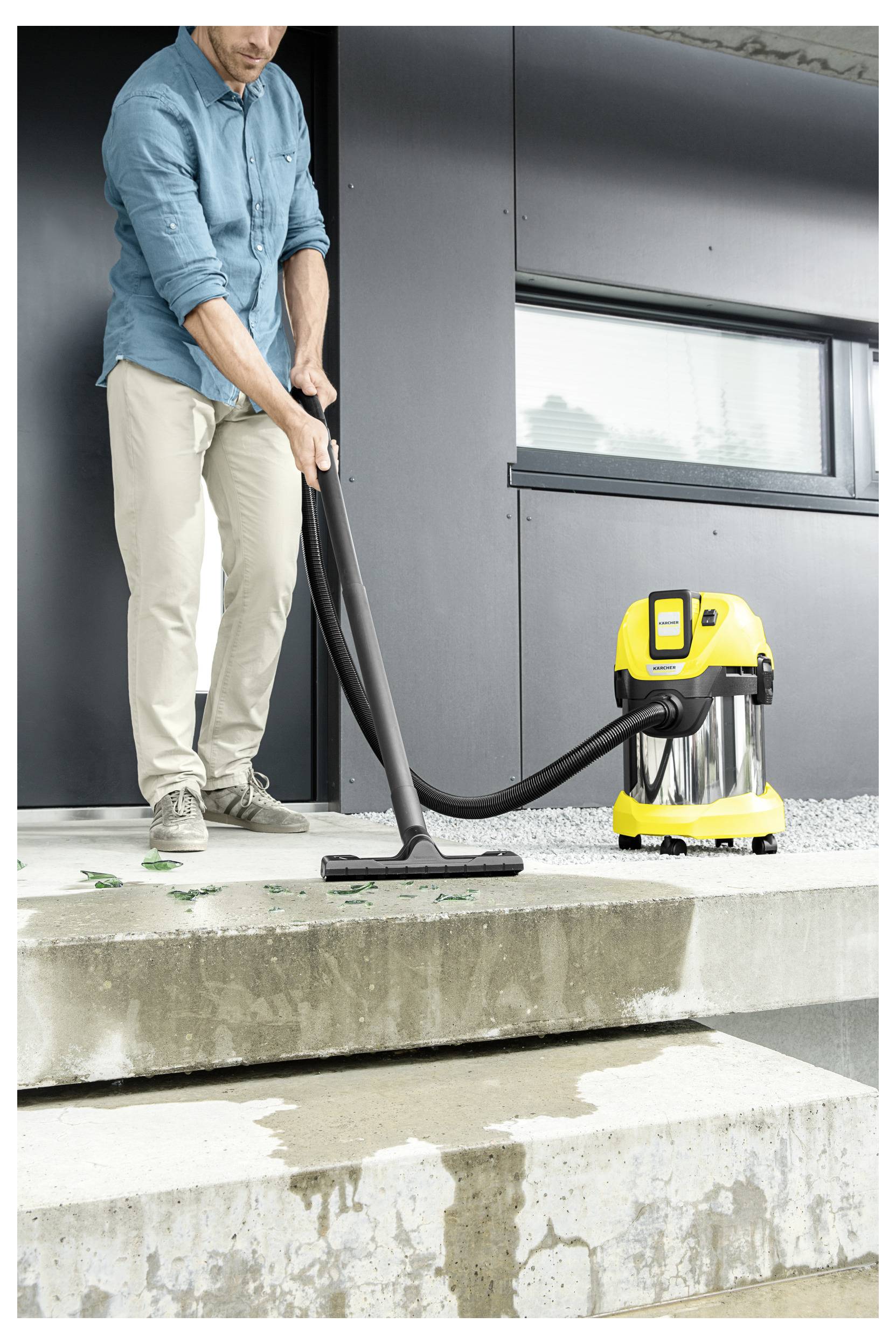 A person using a yellow wet and dry vacuum to clean wet steps outside a building.