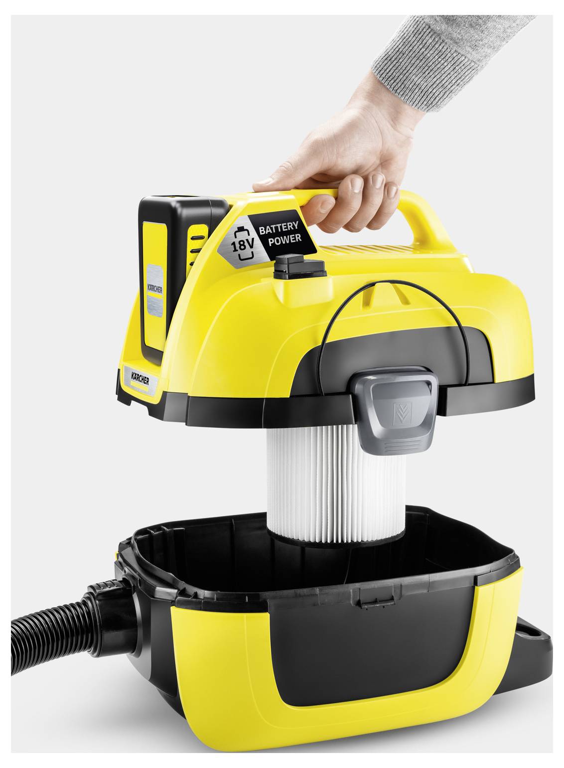 A person lifting the top of a yellow and black portable vacuum cleaner, revealing a white filter inside.