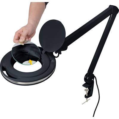 A hand is placing a lens into a round, black magnifying lamp with a long, adjustable arm and a table clamp.