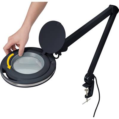 A hand turns the cover of a black, flexible magnifying lamp with a round glass. The lamp has a swivel arm and a table clamp.