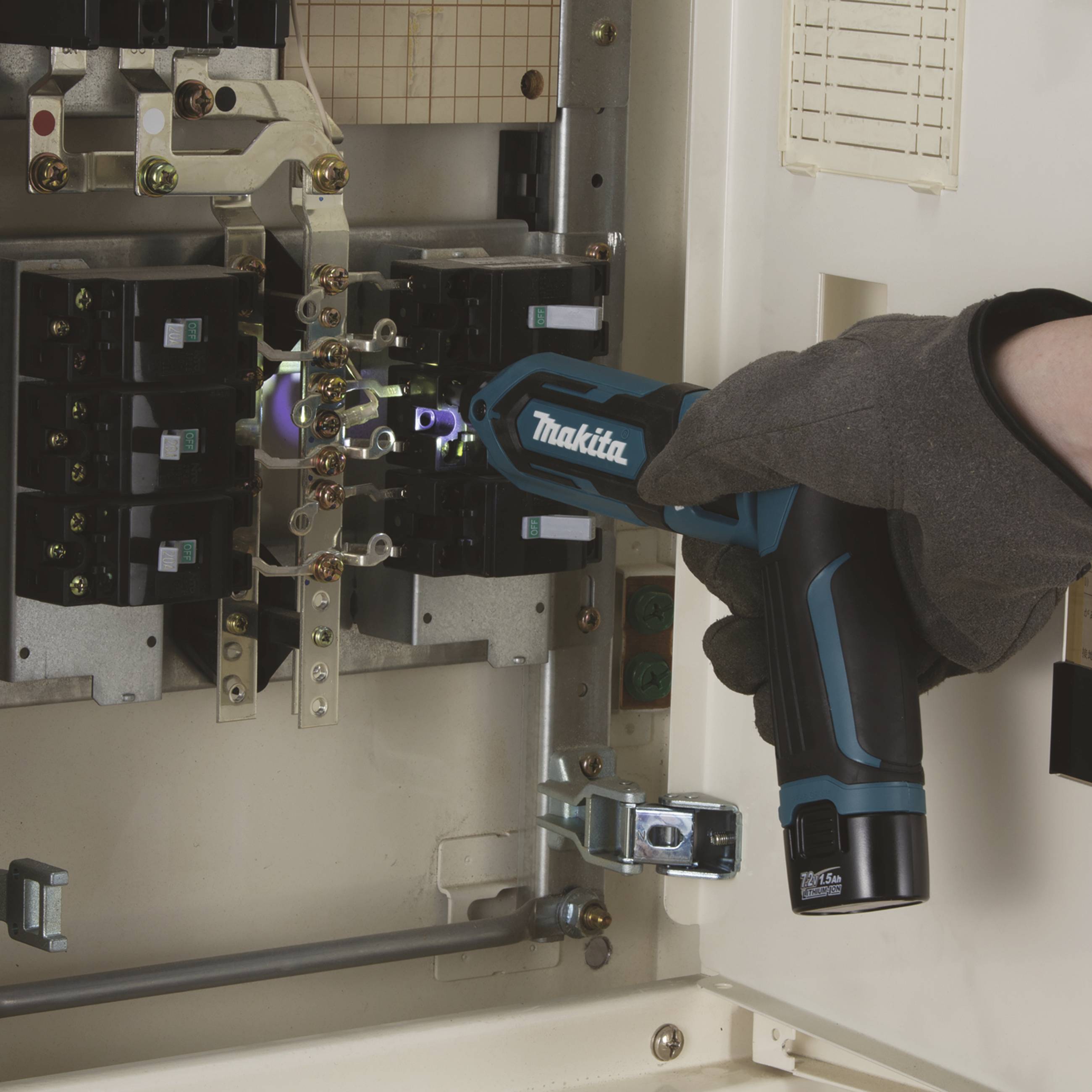 A person wearing a glove is using a blue-black electric tool (brand irrelevant) in an electrical cabinet.
