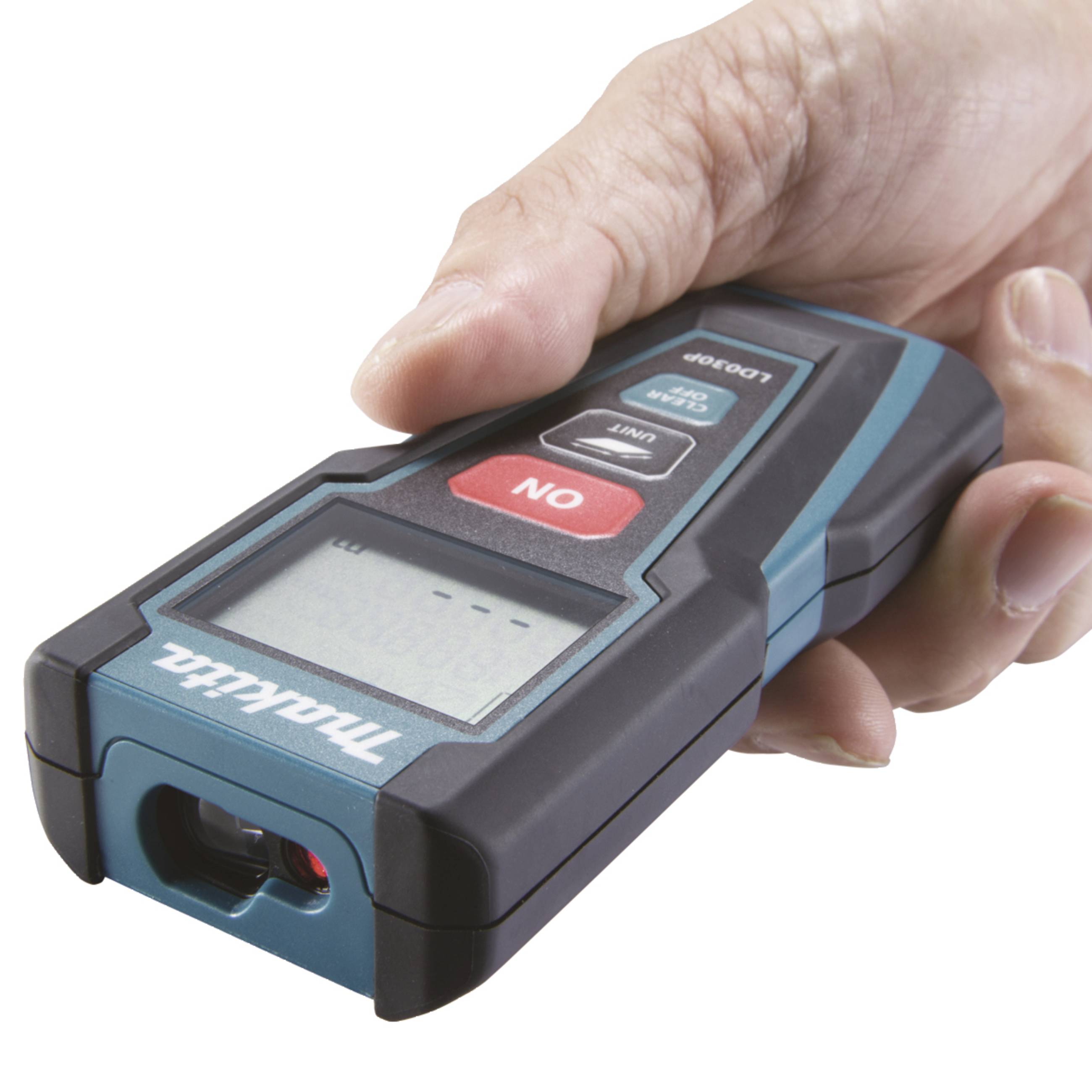 A hand is holding a digital laser distance measuring device with a red 'ON' button and display on the top surface.