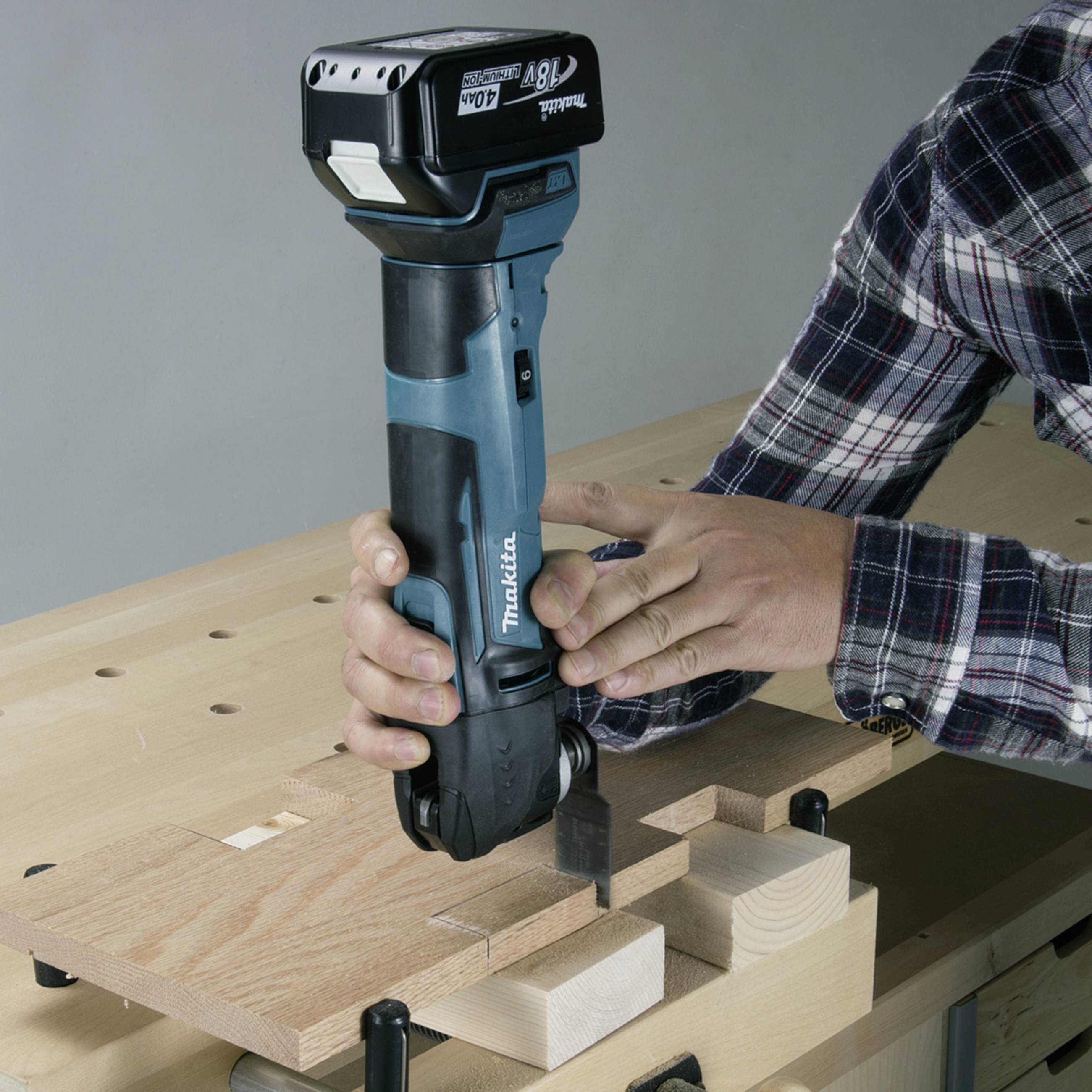 A person is working with a blue cordless drill on a piece of wood on a workbench.