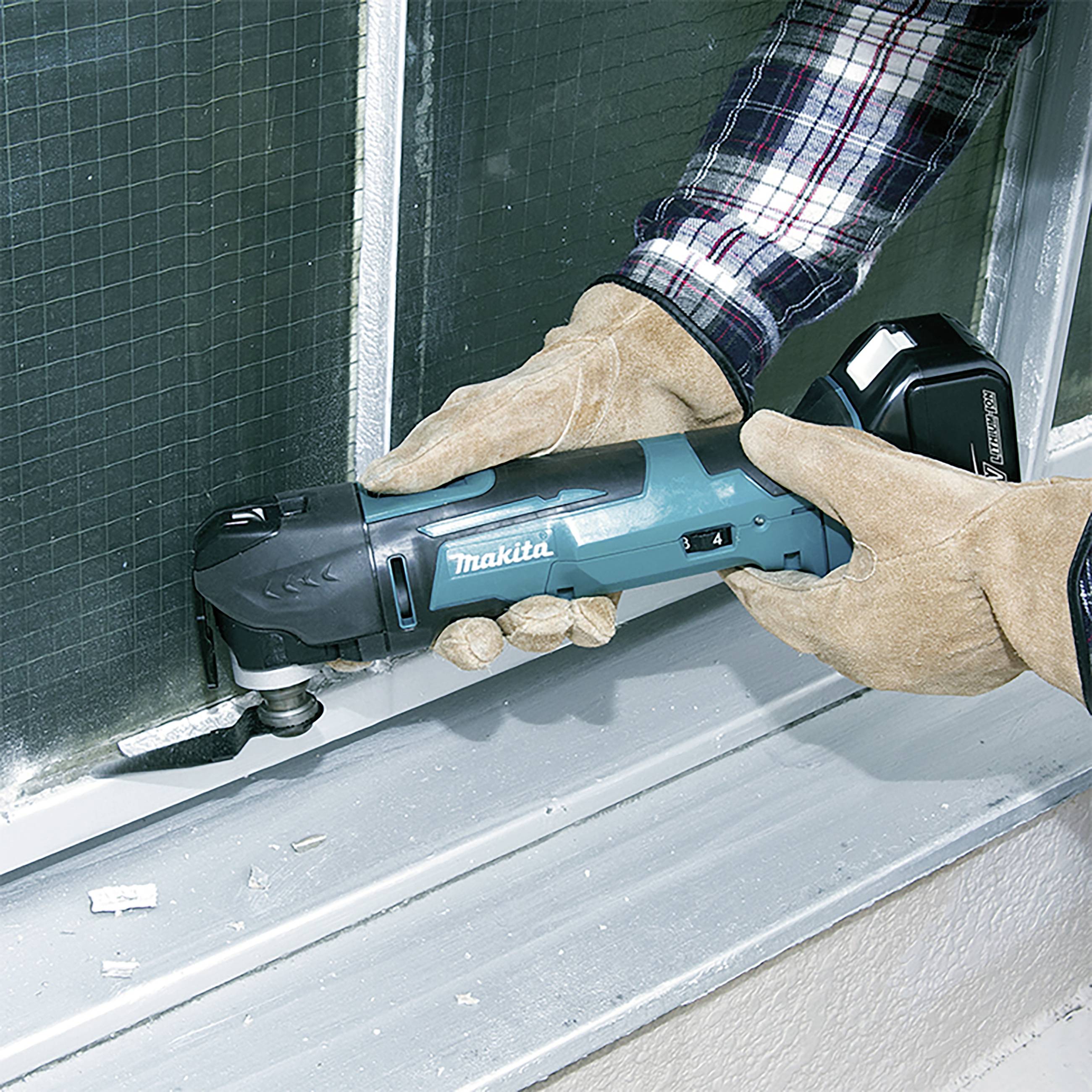 A person is using an electric multi-tool to work on a window frame. They are wearing safety gloves.
