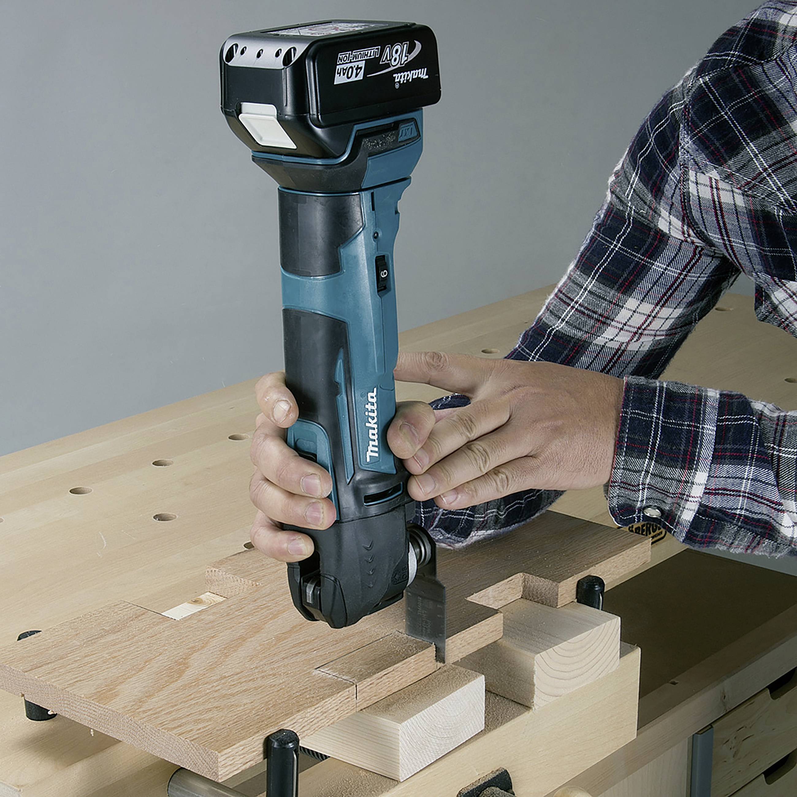 A person is holding a blue machine and routing a groove into a piece of wood on a wooden table.