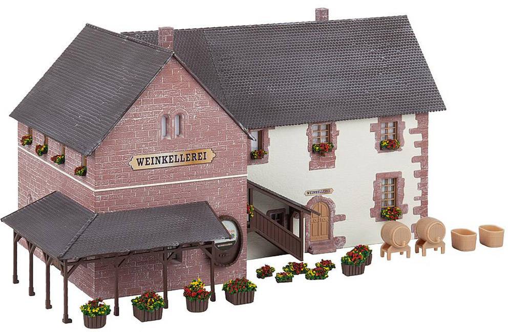 Miniature model of a wine cellar with a tiled roof and barrel storage. Red brick walls and white accents, surrounded by flower planters.