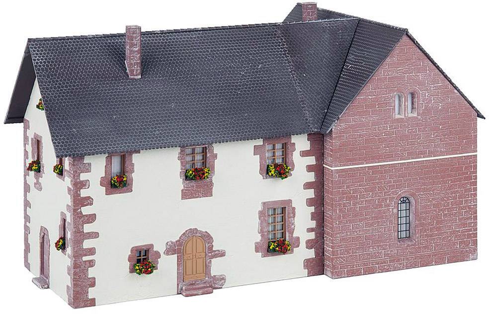 Model house in a traditional style with white walls and red brick accents. Windows with flowers, dark slate roof.