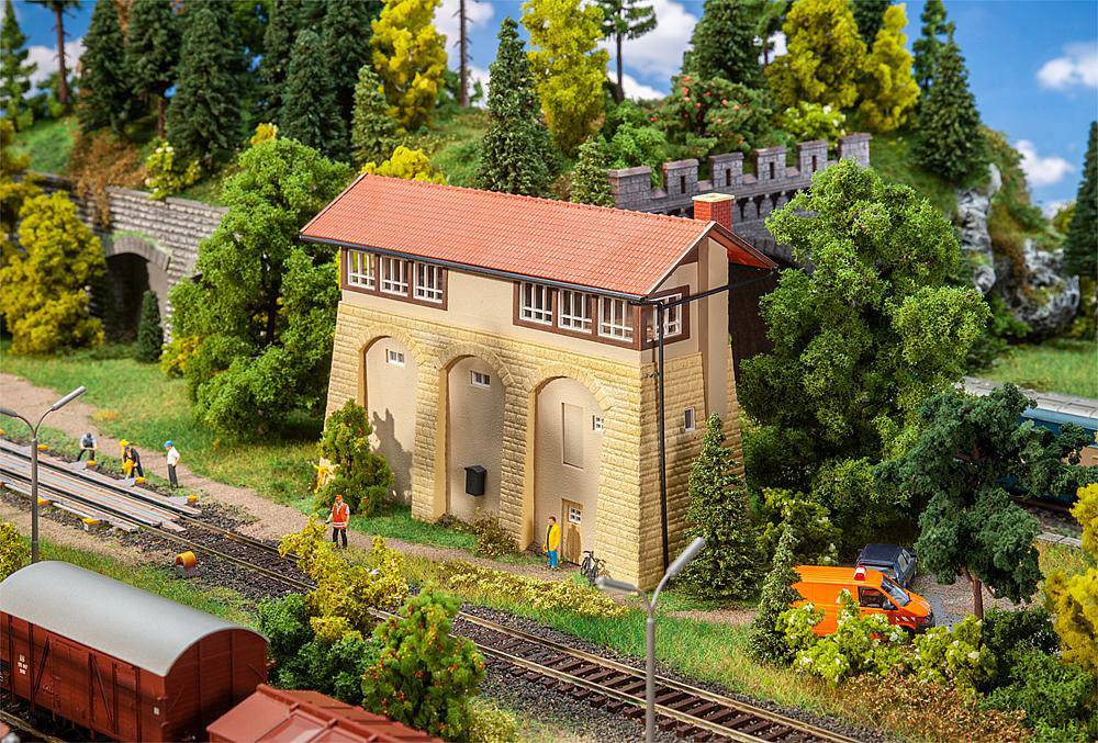 Miniature landscape scene with railway tracks, a water tower, trees and figures. An orange delivery van is parked beside the tracks.