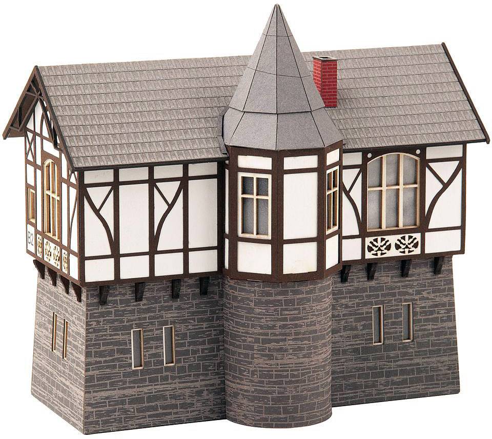 A miniature model of a half-timbered house with a tower, grey roofs, and detailed timber-framed beams on a stone base.