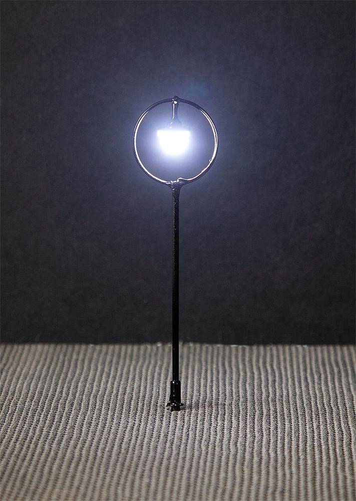 A tiny street lamp with a bright light on a dark background, resting on a textured, grey surface.