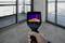 A hand holds a thermal imaging camera, showing temperature differences on the floor in a room with glass walls. Focus on the camera display with colour gradient.
