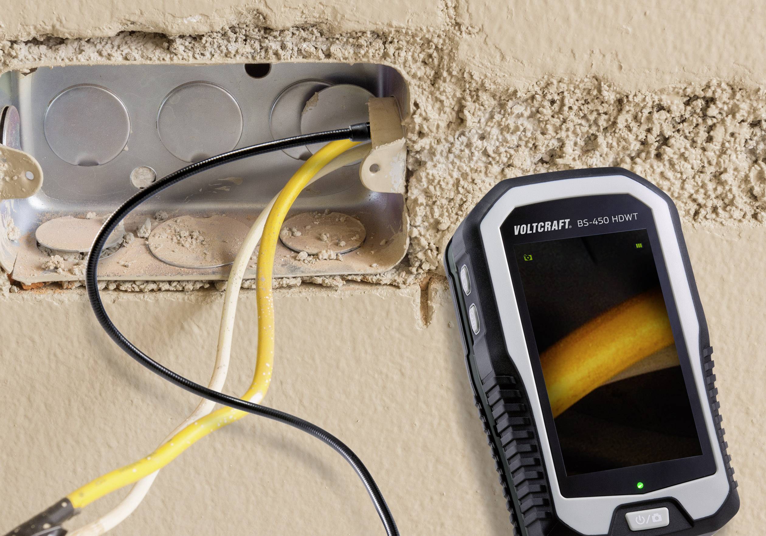 An open socket with exposed yellow cables, next to a handheld device with a screen displaying details of the cable connection.