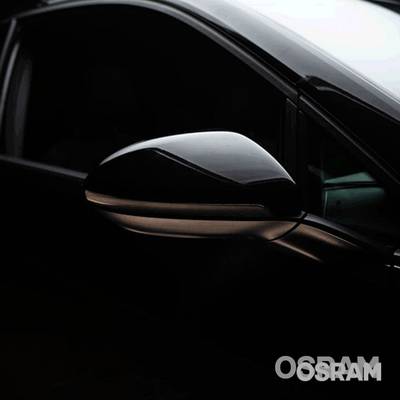 Car wing mirror in black, in focus. The surroundings are dark, which highlights the mirror. The brand name 'Osram' is visible.