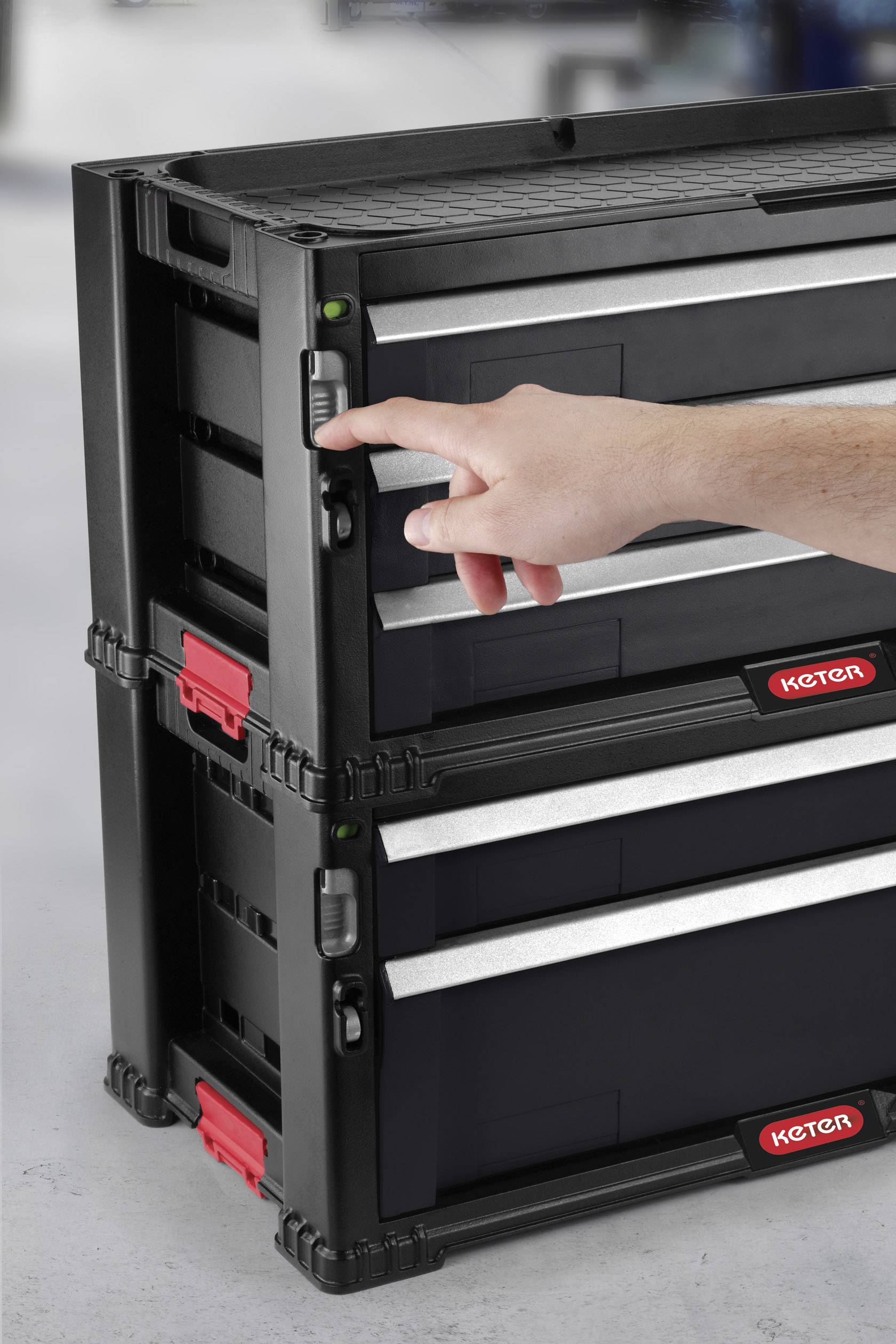 A stack of black plastic containers with red handles. A hand is operating a switch on the side of the top container.