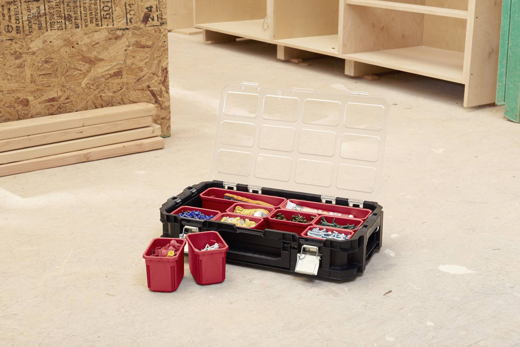 An open toolbox with compartments, filled with screws and wall plugs of various colours, sits on a concrete floor in a workshop.