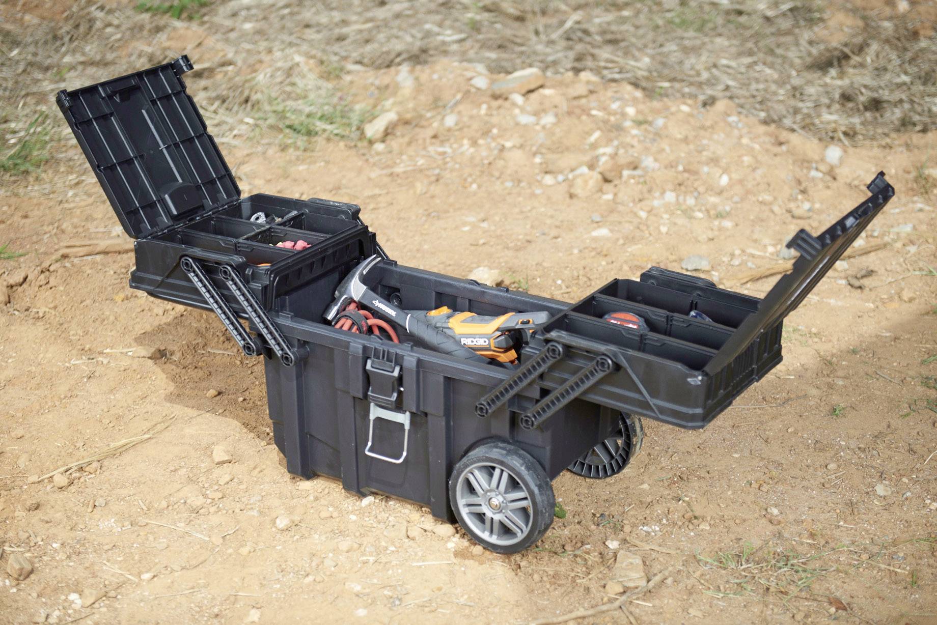 An open toolbox on wheels stands on the ground. It displays various compartments with tools, including an orange drill.