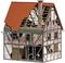 A miniature model of a half-timbered house with a partially destroyed roof and damaged walls, revealing visible bricks and wooden beams.