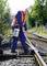 A worker in protective clothing is spraying a substance onto railway tracks for maintenance. Trees and additional tracks can be seen in the background.