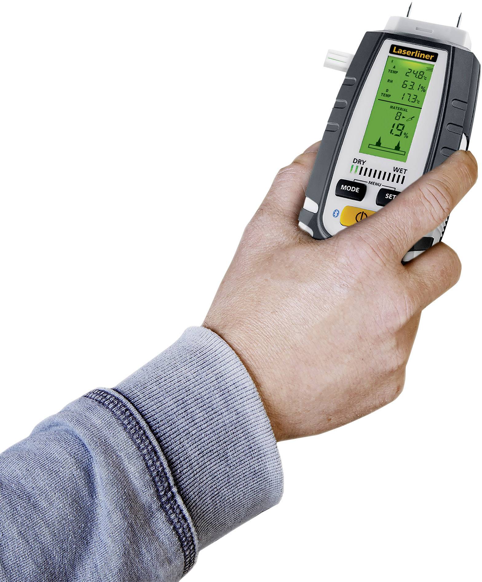 A handheld moisture measuring device is being held by a person. The display shows several measurement readings.