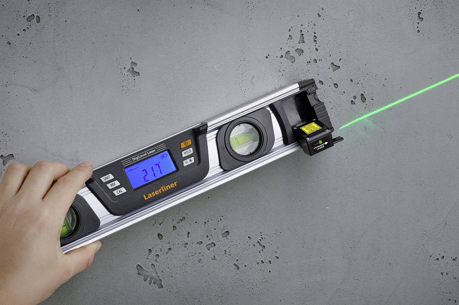 'A hand is holding a digital spirit level with laser, which is being aligned against a concrete wall. The laser beam is projecting a green line.'