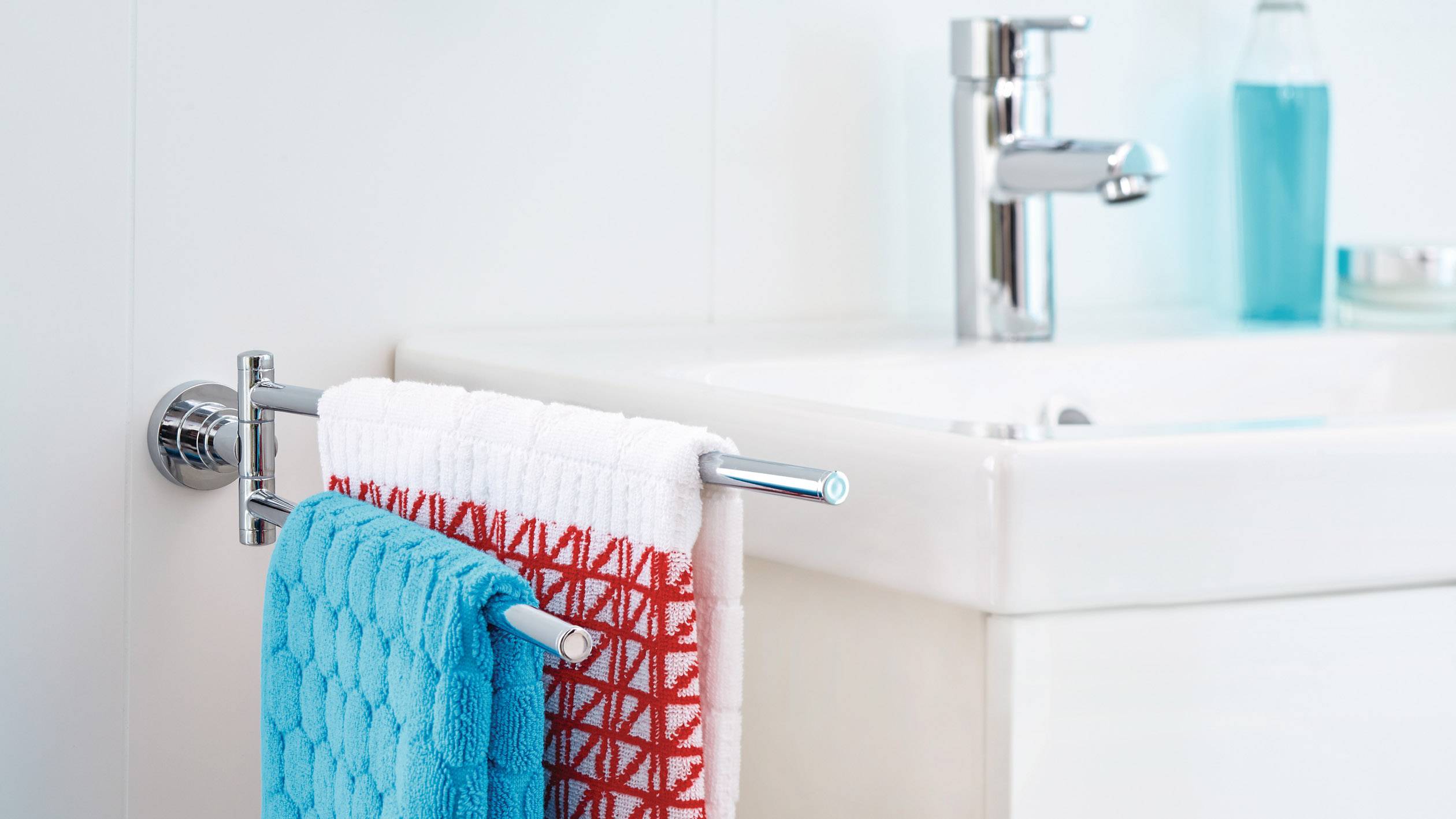 A bathroom with a towel rail beside a washbasin. Two towels are hanging: one blue, one red and white patterned.