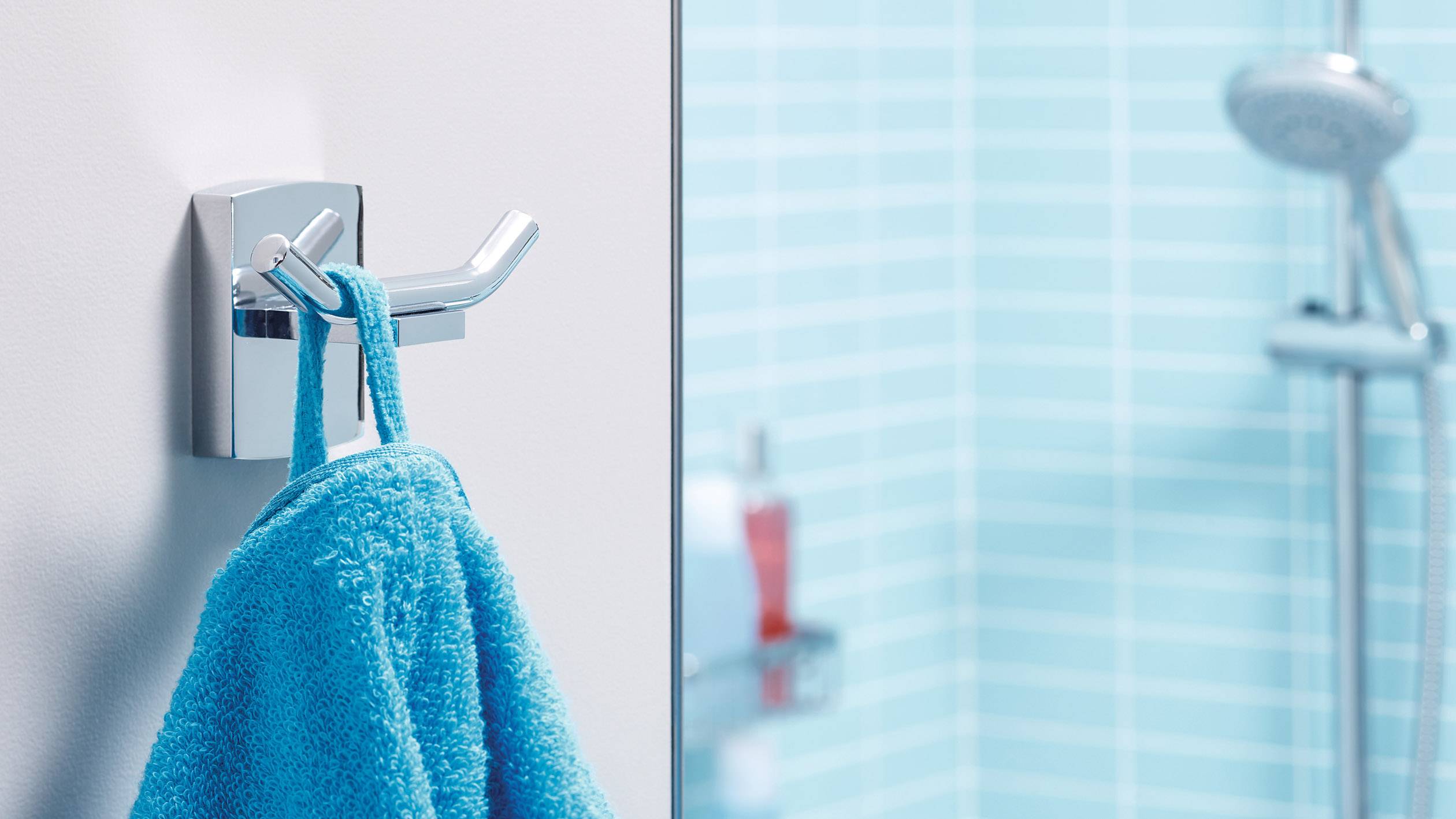 A blue towel hangs on a silver hook in front of a blue-tiled shower.