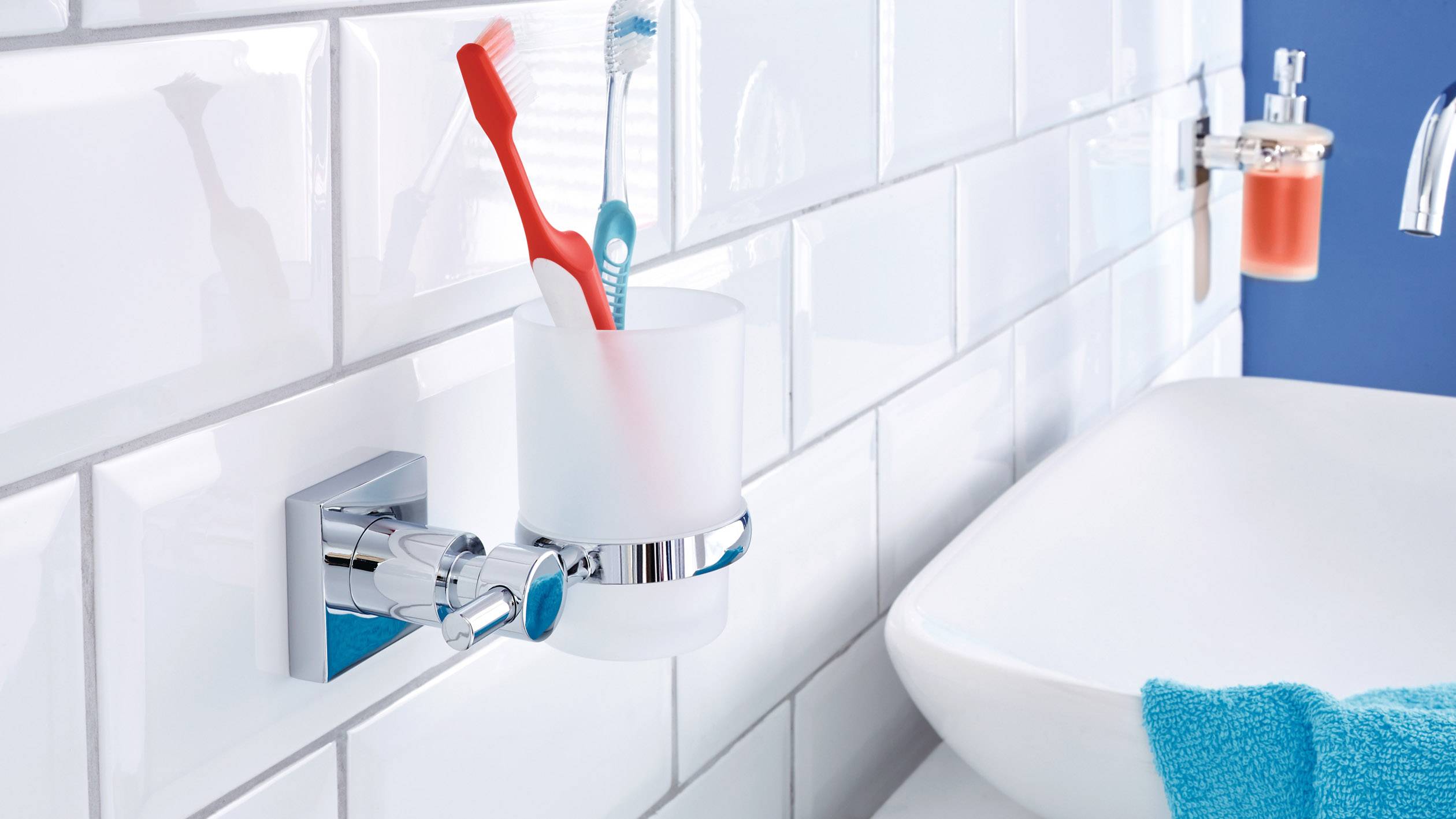 Two toothbrushes in a holder on the tiled bathroom wall next to a washbasin.