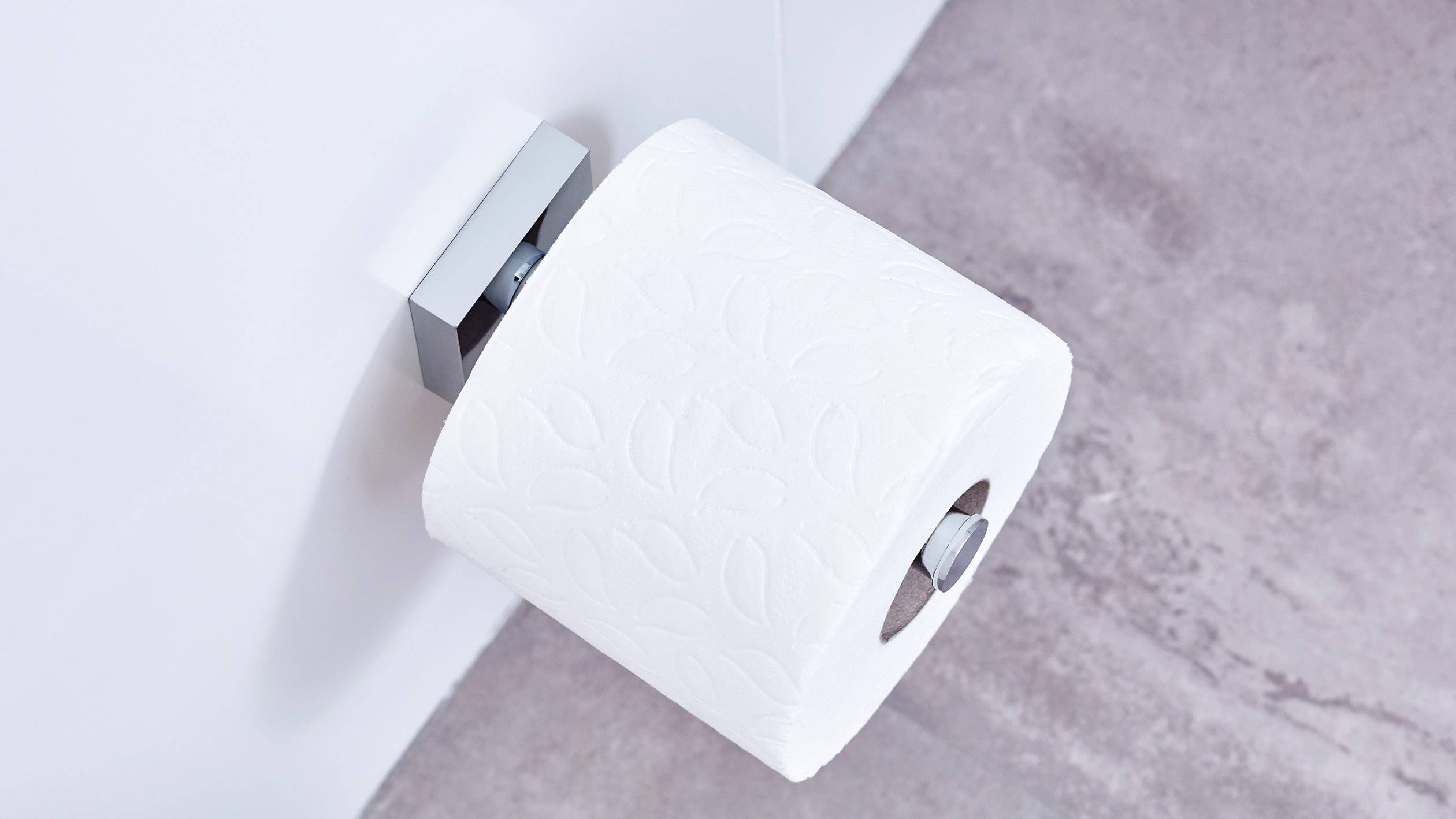 A roll of toilet paper hangs on a modern, silver wall holder against a pink tiled wall.