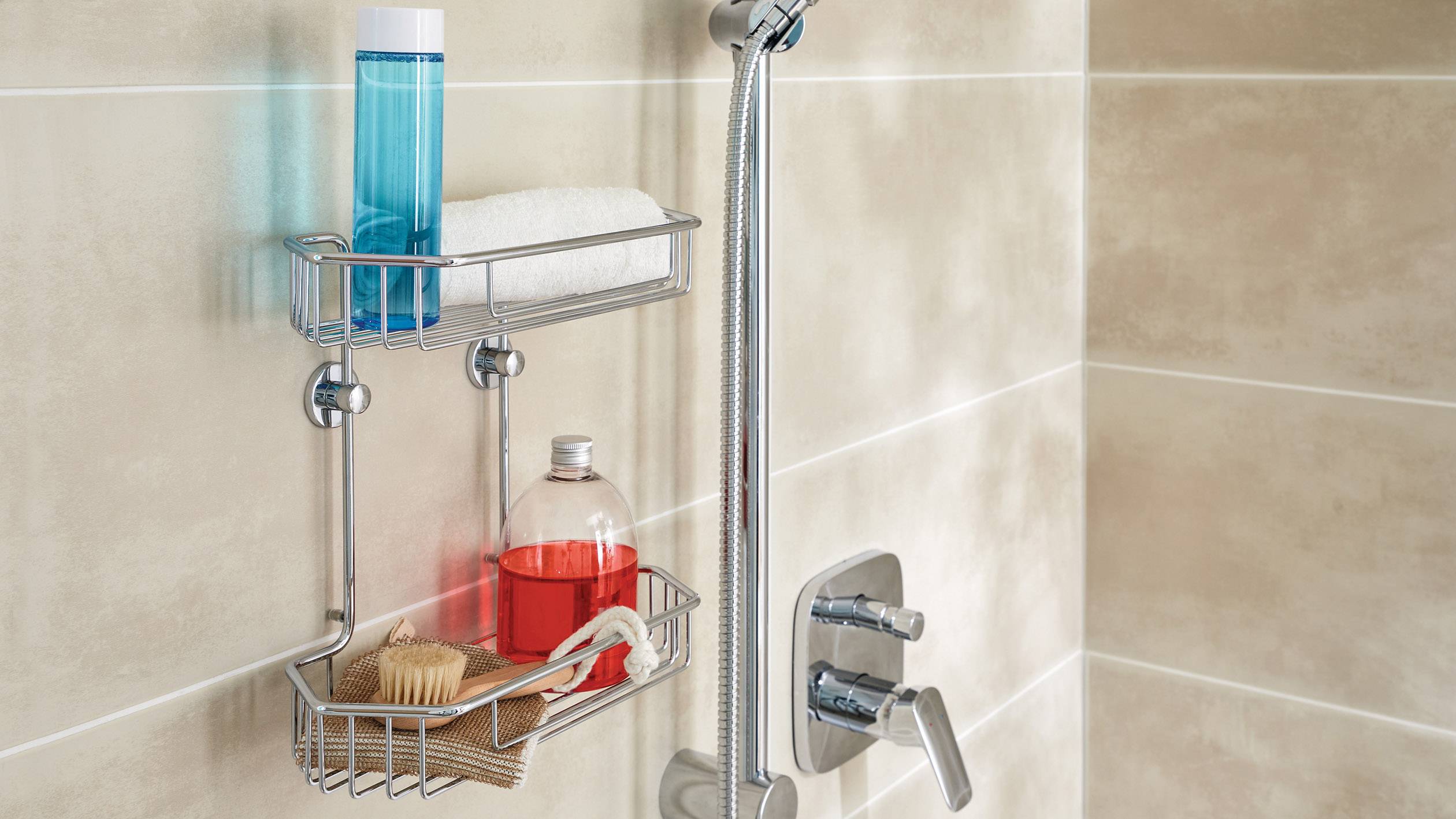 Shower head and shower shelf with blue bottle, red container, brush and soap on tiled wall.