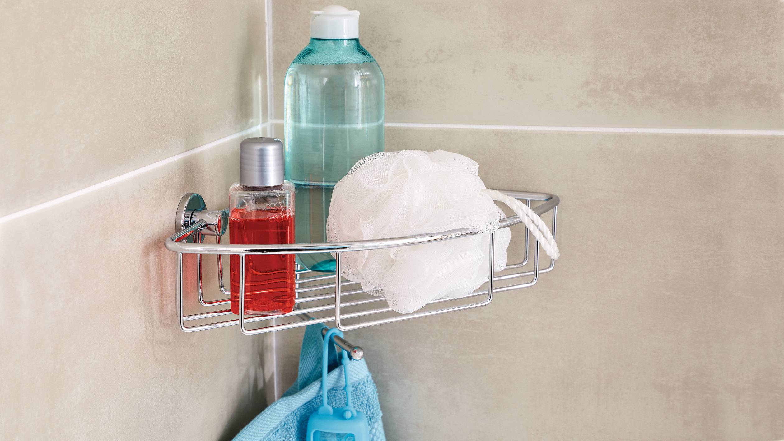 Shower shelf with blue and red shower gel, sponge and towel in a light-tiled shower.