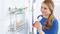 A woman in blue clothing stands in a bathroom and holds a red bottle. Toiletries are situated on a shower shelf.