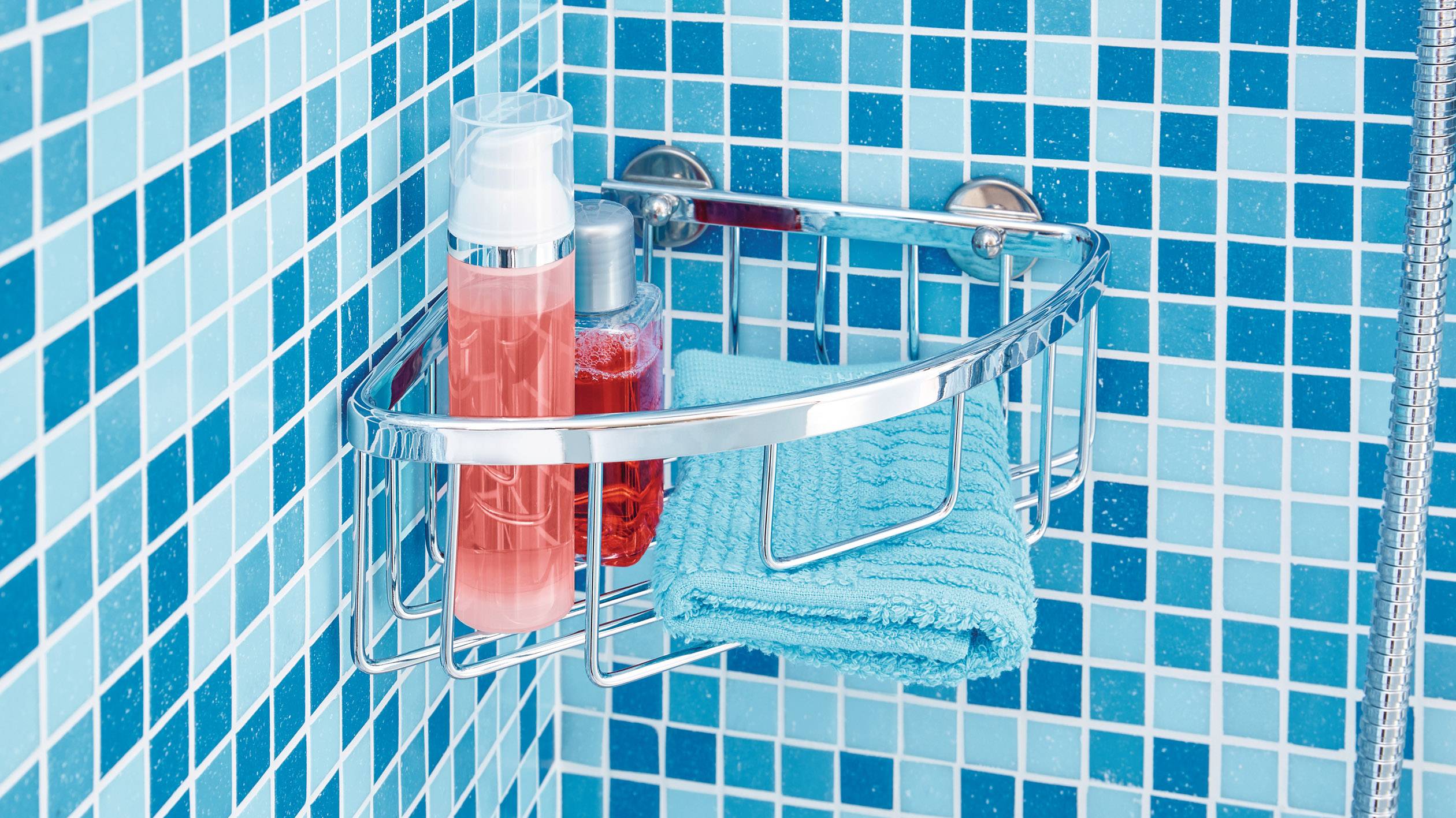 A shower shelf with blue tiles in the background contains two shower gel bottles and a folded blue towel.