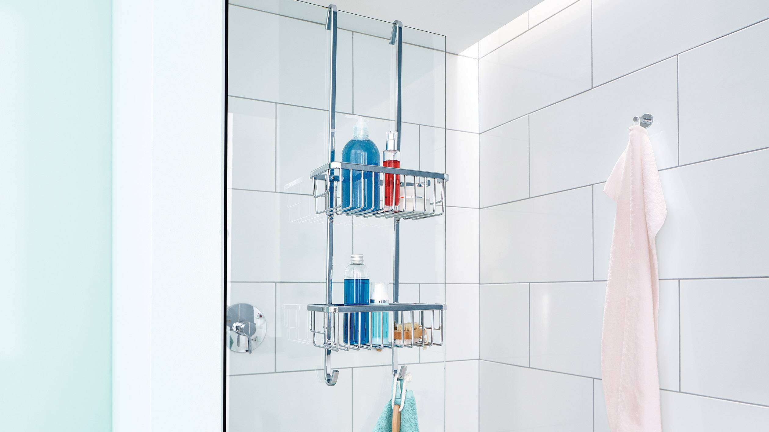 A metal shower basket organiser hangs on the tiled shower wall. It is decorated with blue toiletries and a pink towel roll.