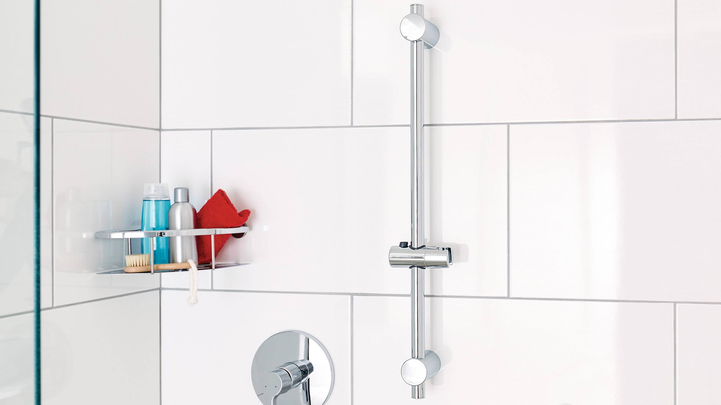 Shower enclosure with an adjustable shower head holder and a shelf corner with shampoo and shower gel bottles, sponge, and brush.