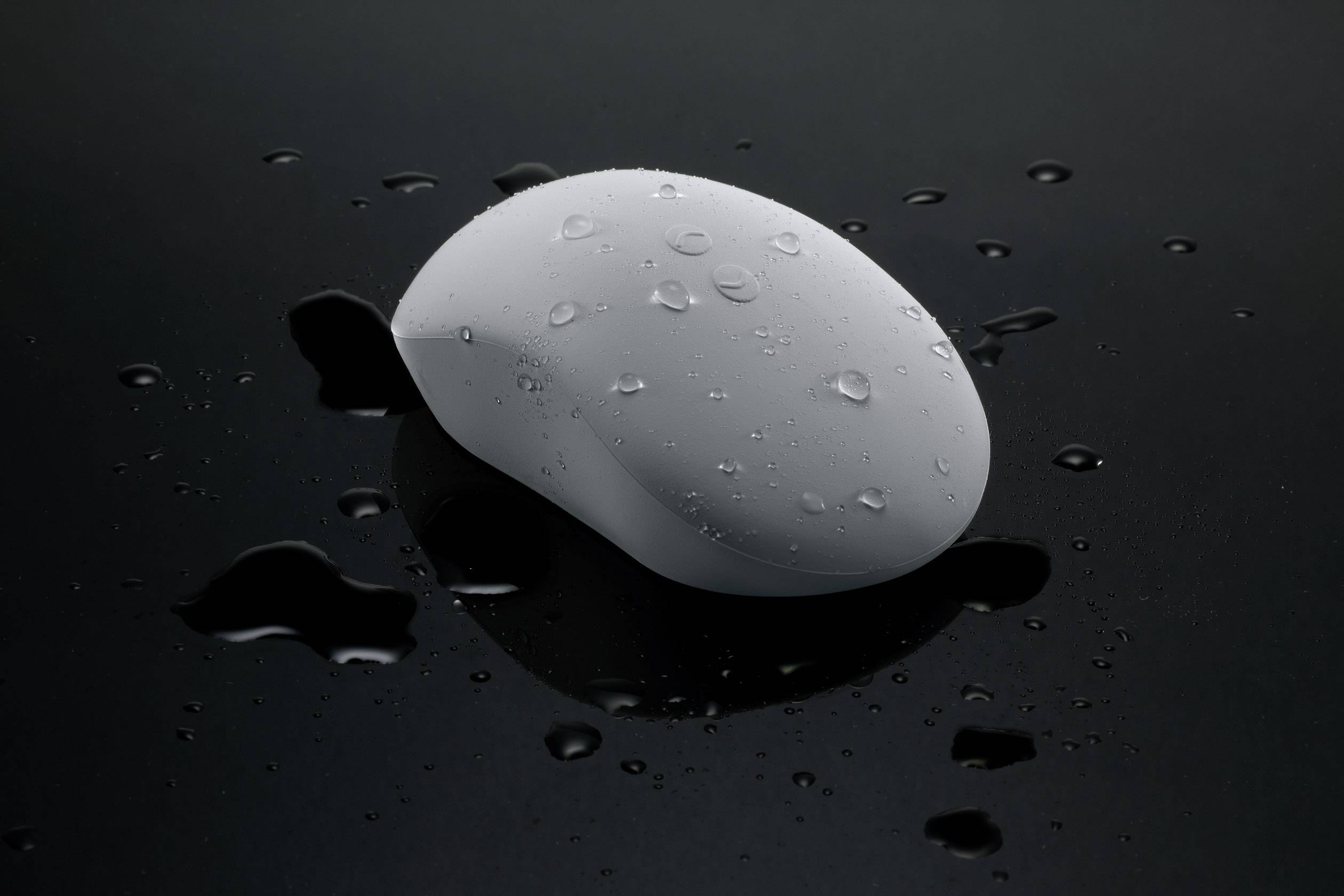 A white oval soap bar rests on a shiny, wet surface. Water droplets are visible on the soap and around it.
