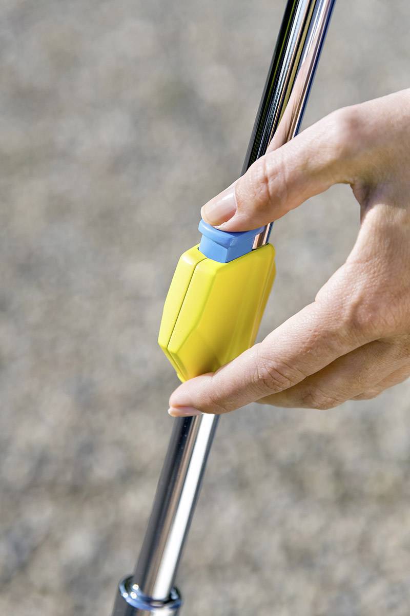 A hand is pressing a blue button on a yellow device mounted on a metal pole.