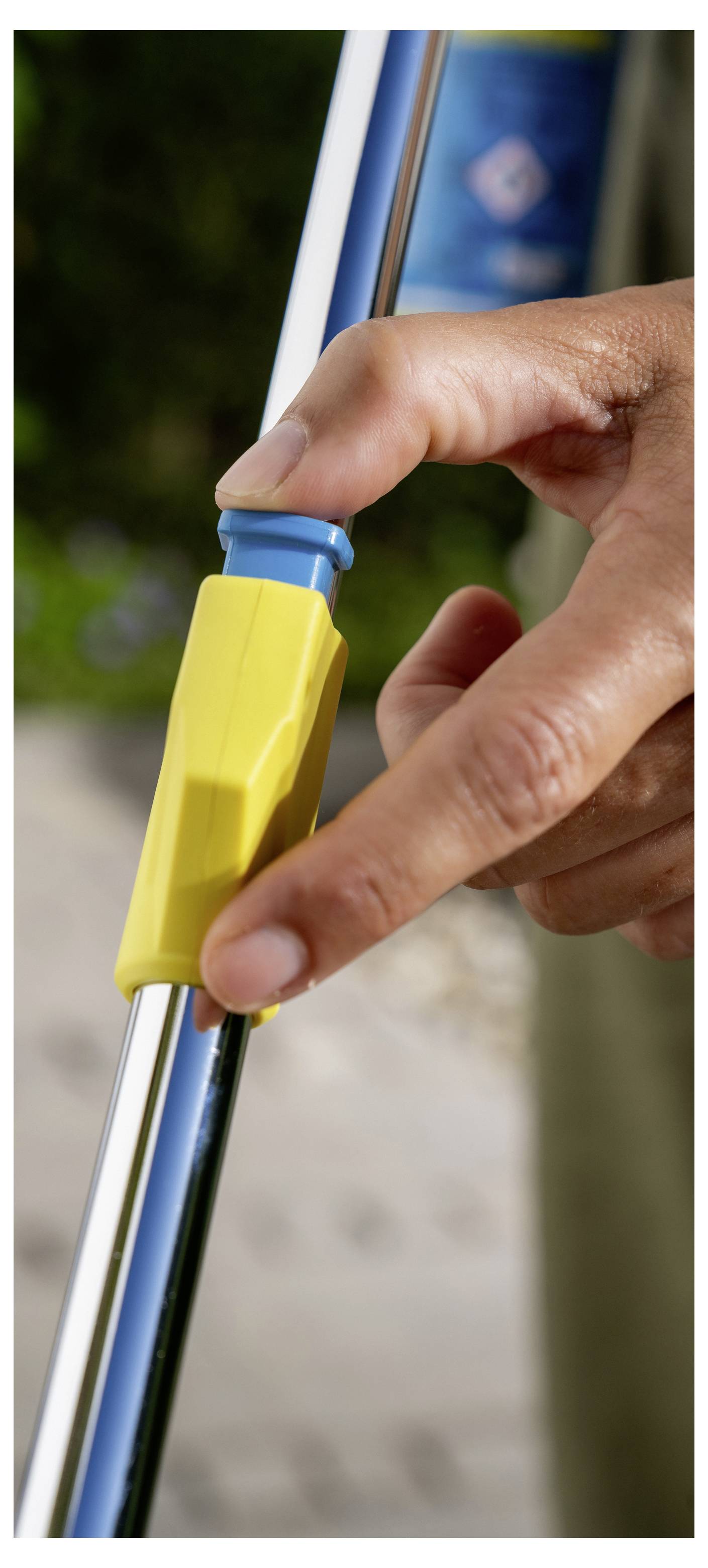 Close-up of a hand sliding a yellow clamp on a metal pole outdoors.