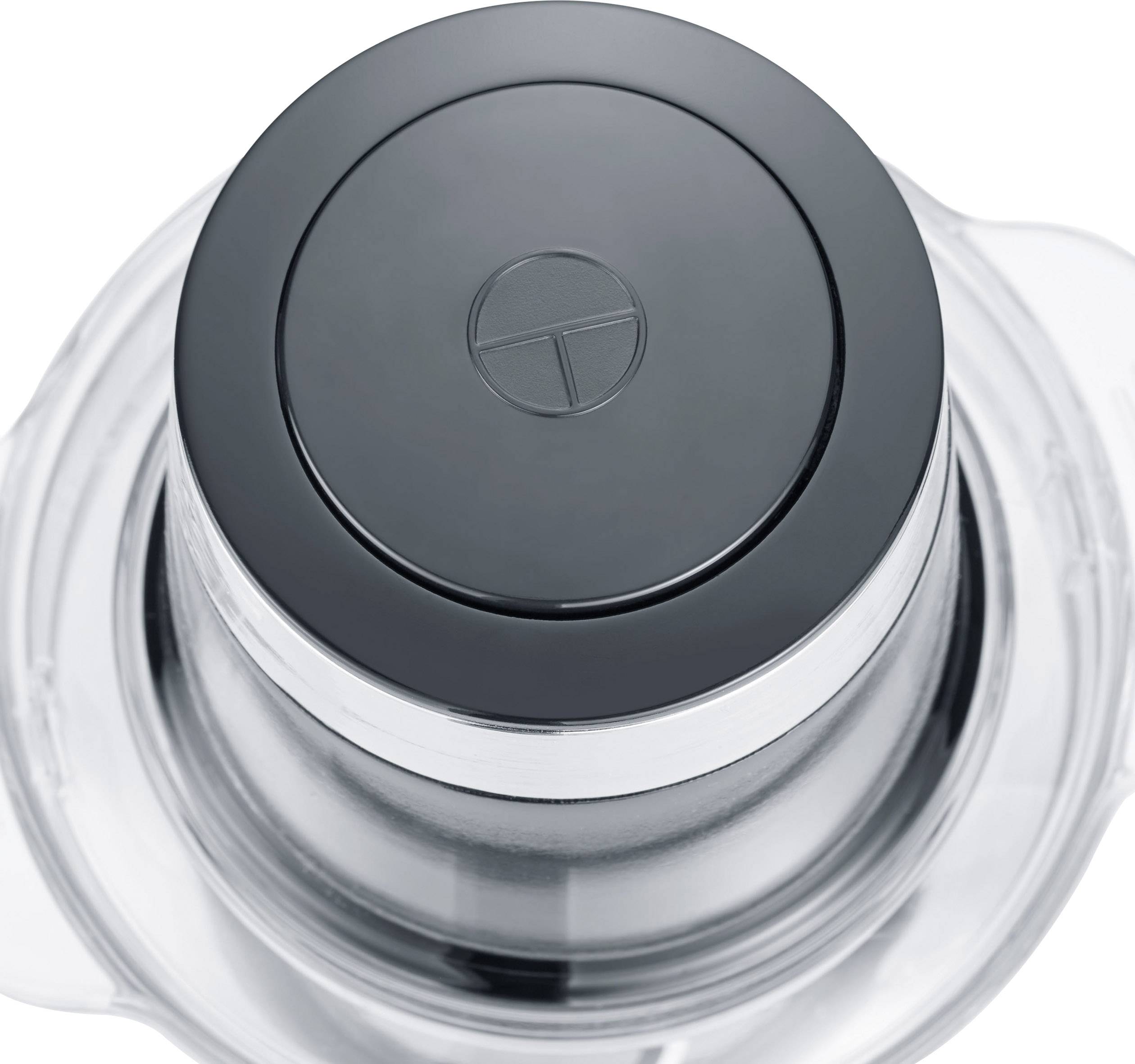 Lid of a kitchen appliance with a black button in the centre. Clear cover and metal fastening visible.