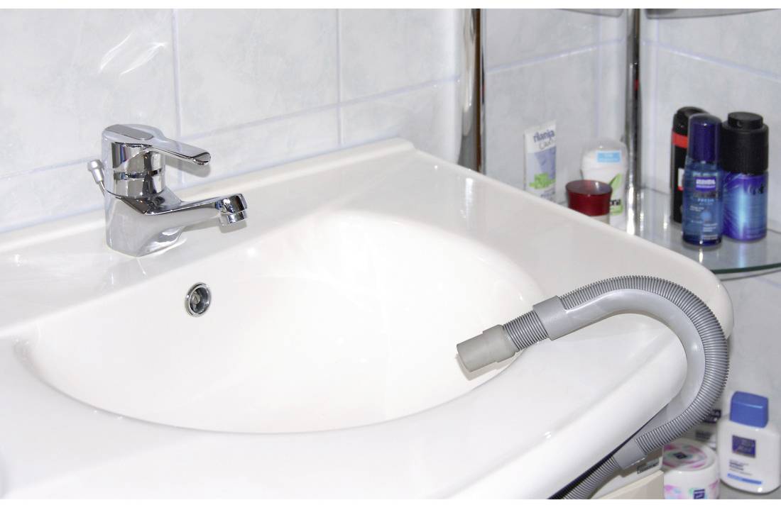 A sink with a vacuum cleaner hose placed into the plughole. Bathroom items are positioned around the sink.