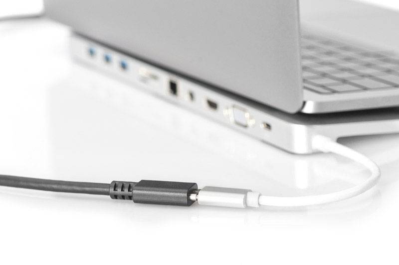 A laptop on a table with various ports; a black audio cable is being plugged into the headphone socket.