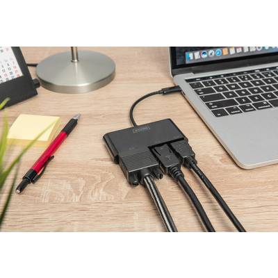 A desk with a laptop, to which an adapter with multiple cables is connected. Beside it are a pen, notepad and lamp.