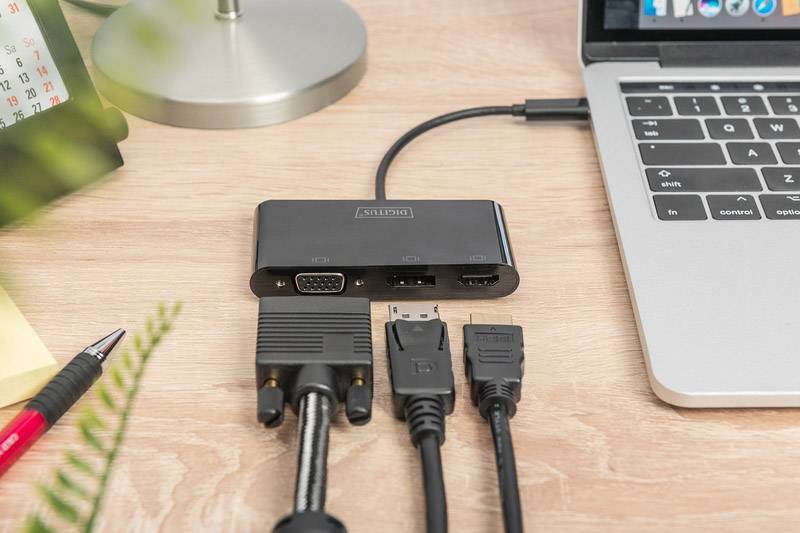 A laptop is connected via an adapter with multiple cables. The adapter provides VGA, HDMI, and DVI ports for different connections.